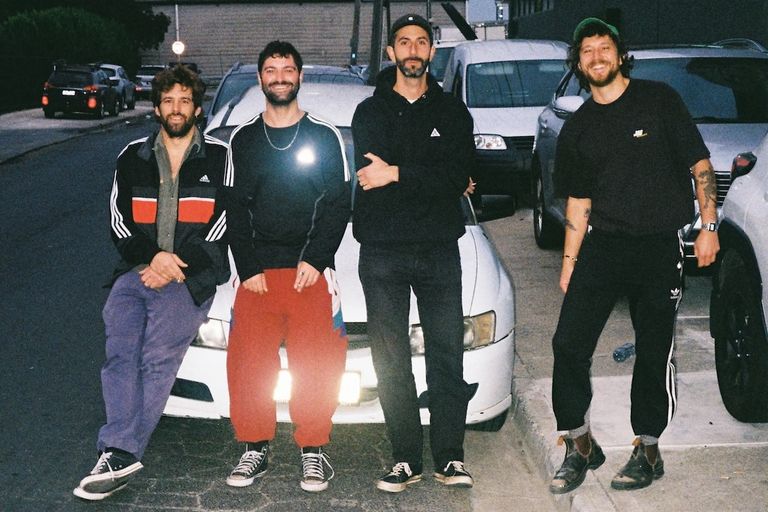 Australian rock band The Pretty Littles posing outdoors in casual street wear, leaning against cars on a city street at night.